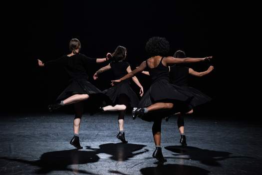 Four dancers swivel on one leg, balancing on the tips of their shoes.