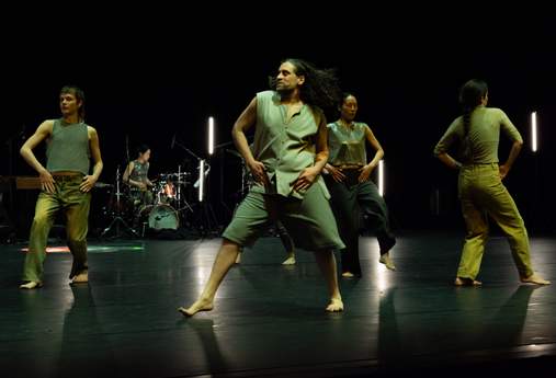 Four dancers move in different directions in a homolateral fashion, each with hands resting on their hips.