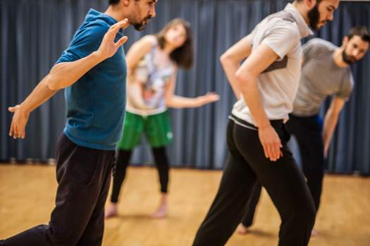 Four dancers lean to the right in synchronized tilt, their individual movements varying.