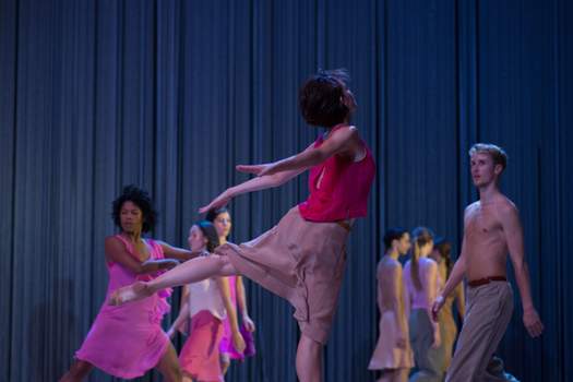 One dancer is caught mid-leap in the foreground, as others move in lines intersecting across the stage.