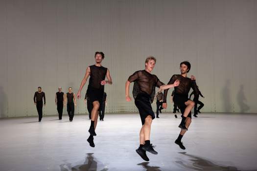 In the foreground, three dancers leap into the air, with two groups of dancers moving or skipping in the background.