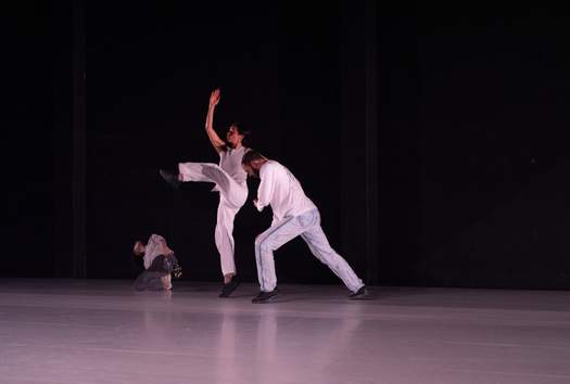 Three dancers reach outward into different parts of the space, their bodies stretching through broad, expansive motions.