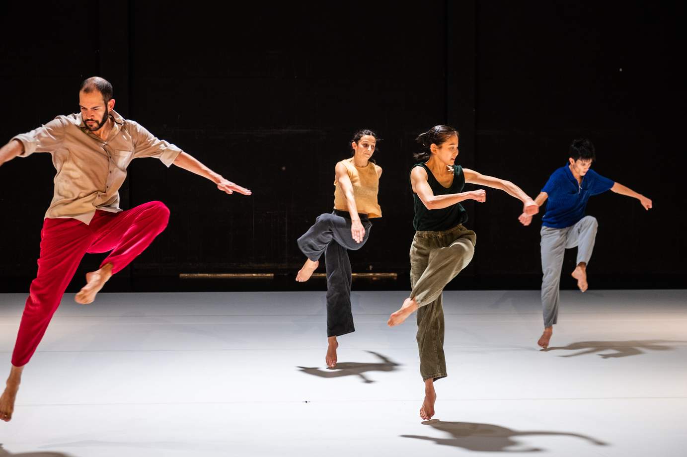 Four dancers wearing colorful costumes are captured mid-jump in unison.