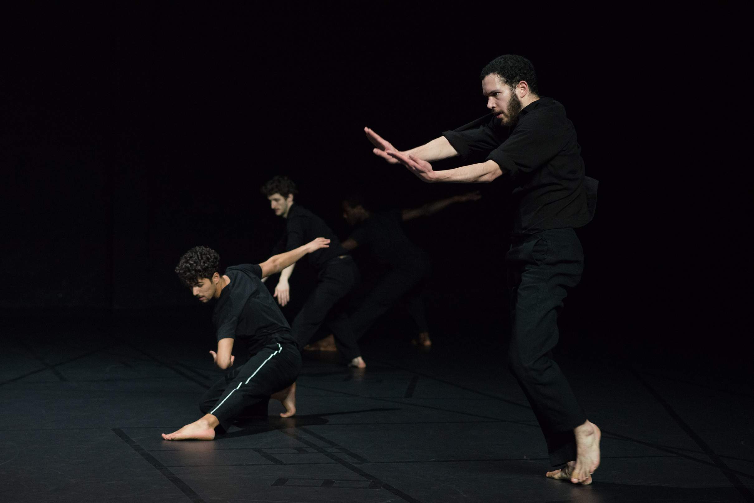 One dancer improvises with fervor in the foreground, while three others mirror similar shapes in the background.