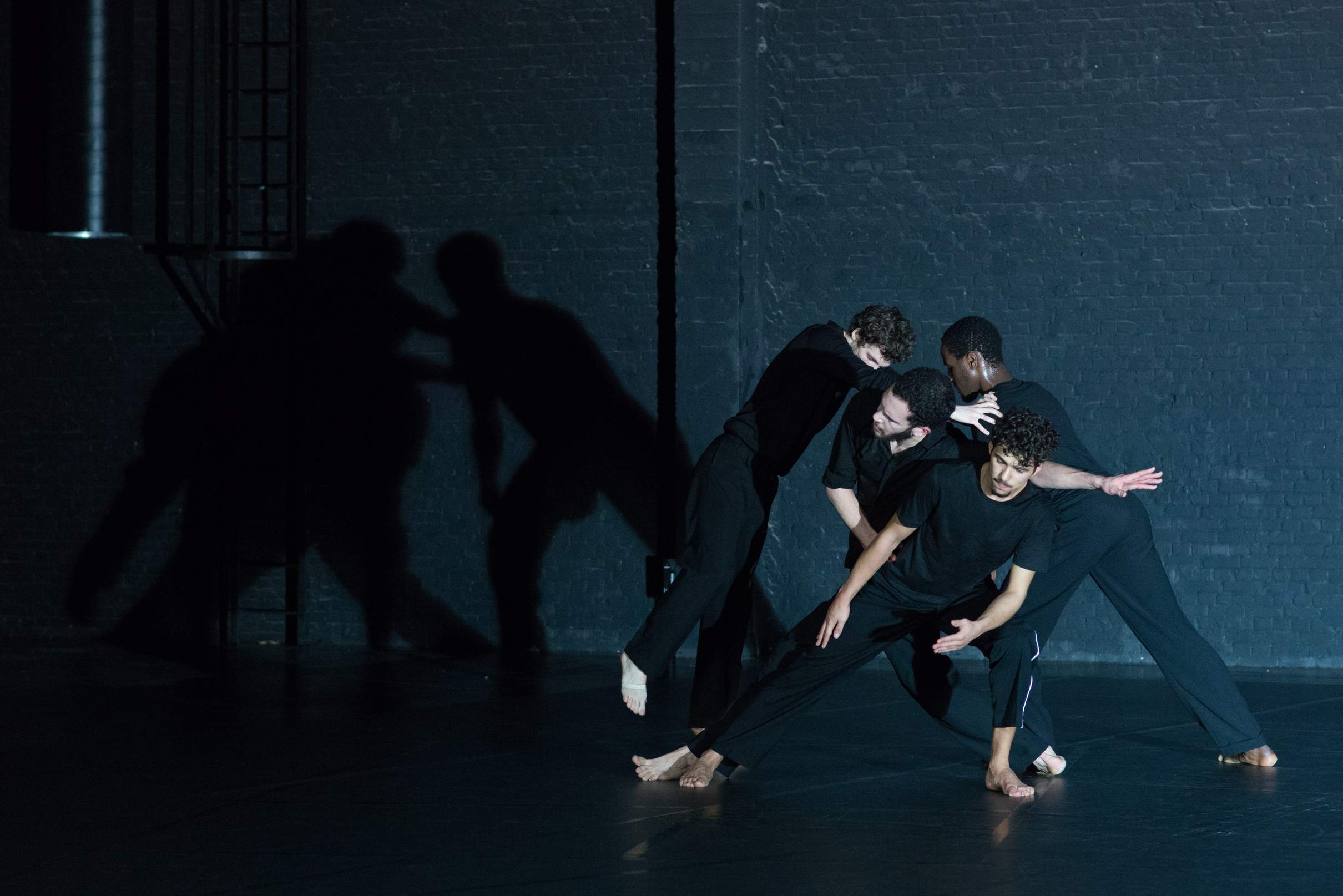 A group of four dancers creates an intricate structure, balancing each other’s weight, with one dancer elevated above the rest.