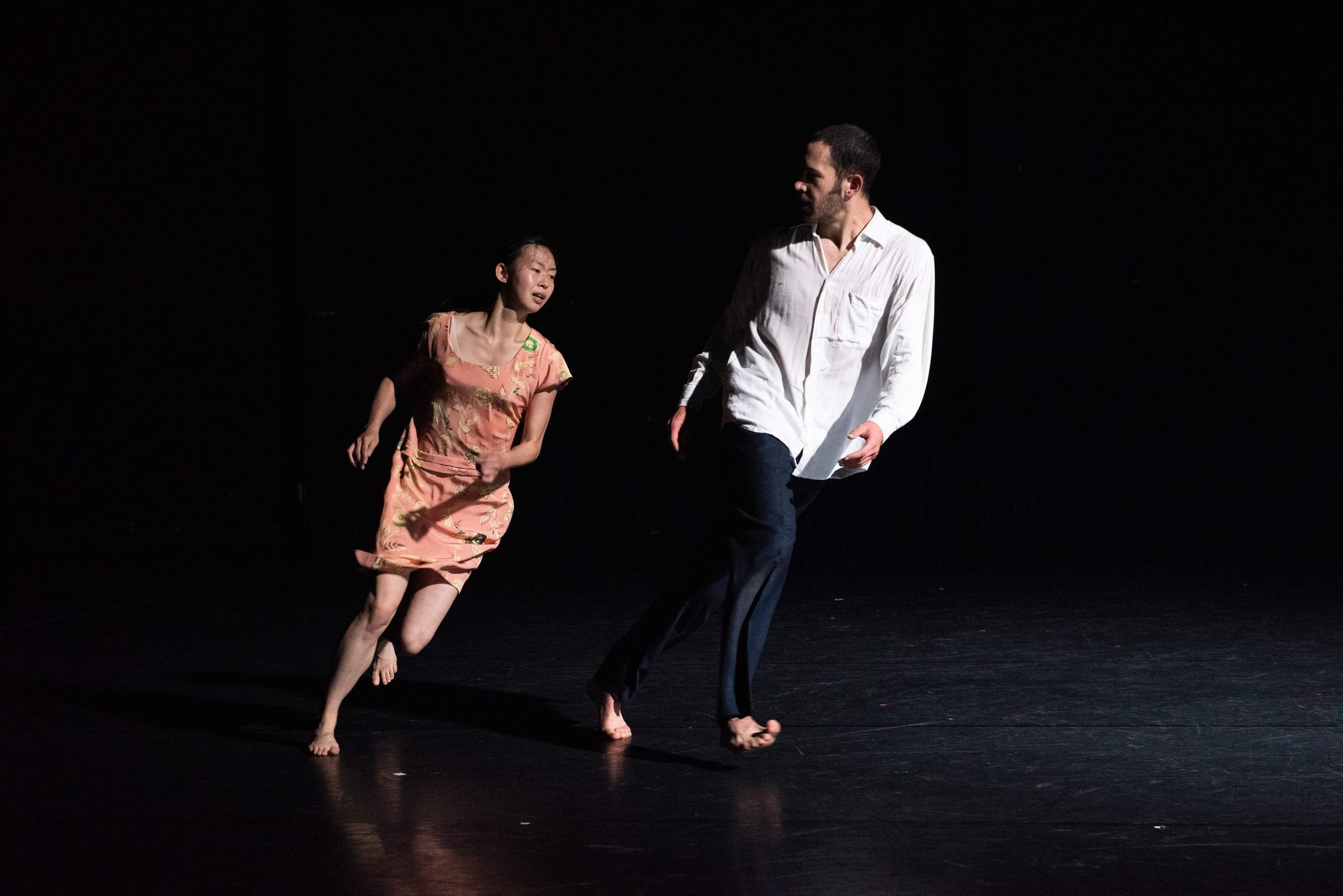 A male and female performer run side by side in an arc, the man poised to catch the woman.