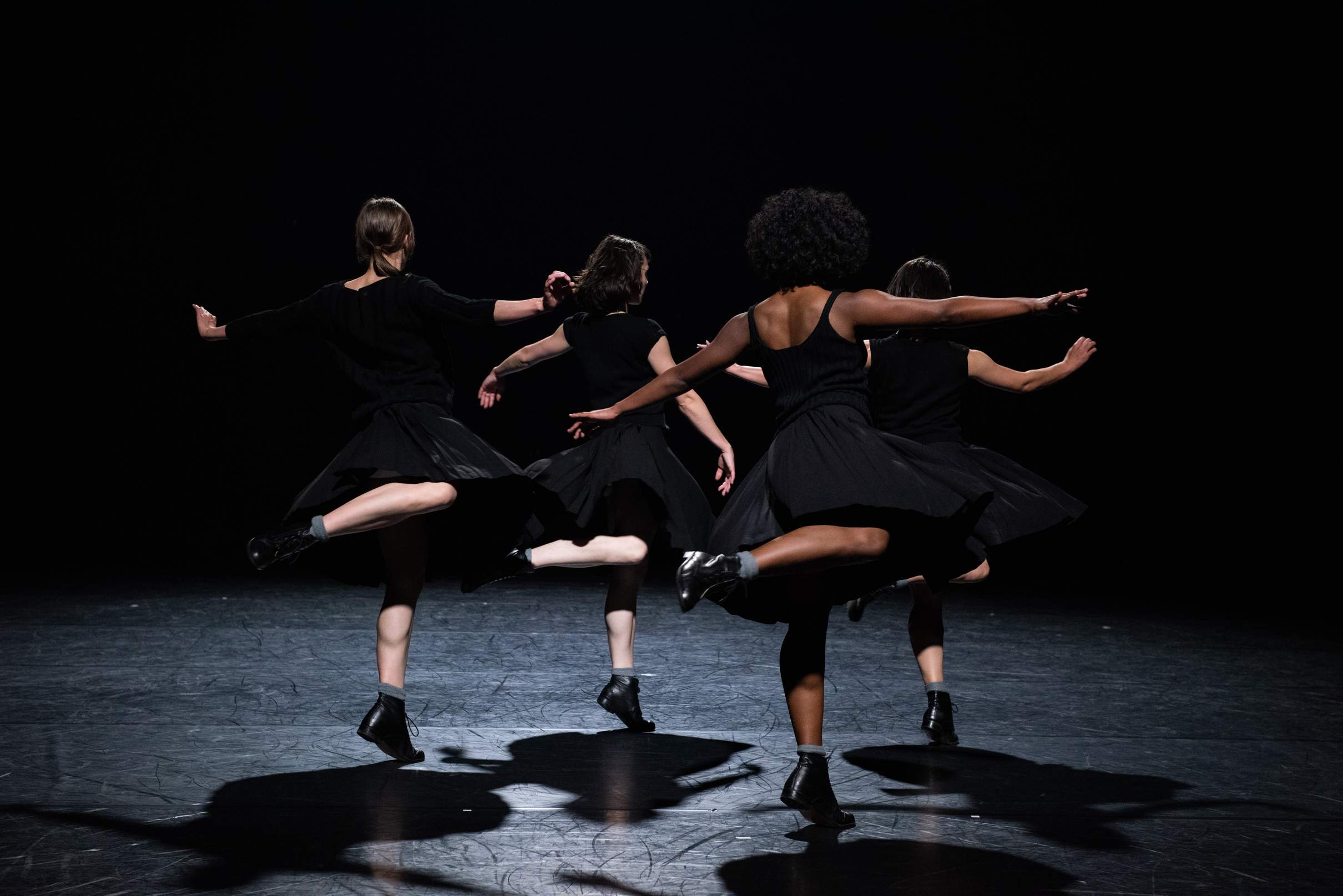 Four dancers swivel on one leg, balancing on the tips of their shoes.