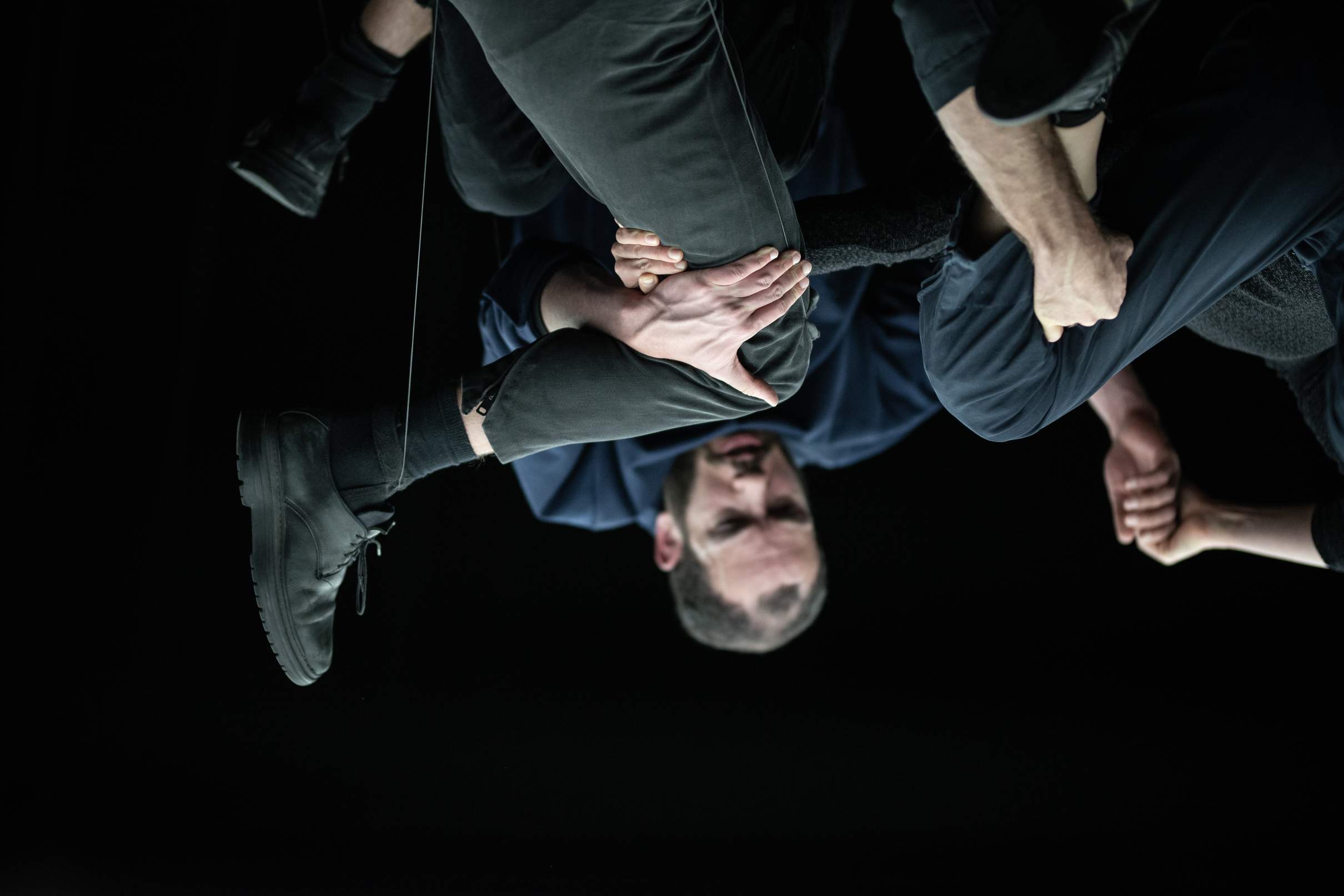 Three performers cling to one another in midair, forming a dense tangle where individual limbs and bodies are barely discernible.