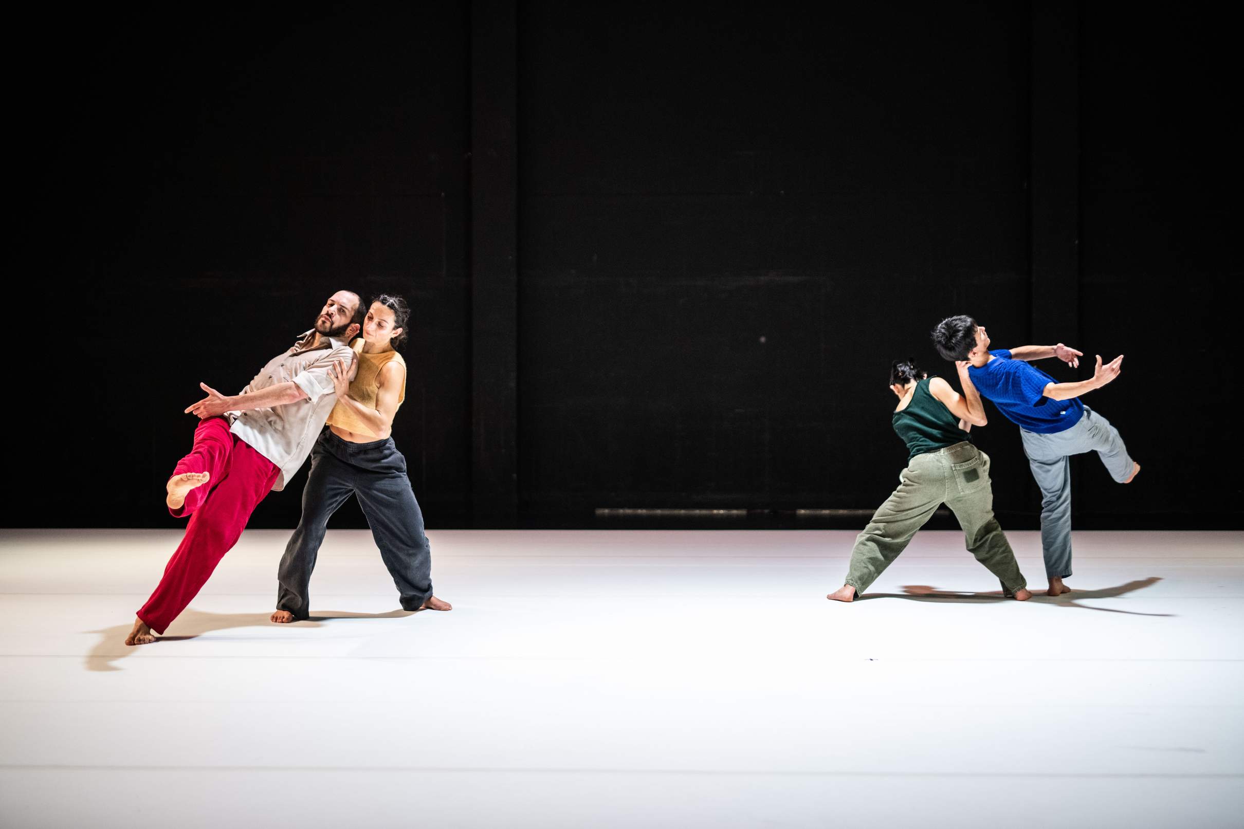 Two pairs of dancers perform a synchronized duet on opposite sides of the stage, with the women holding the men off balance.