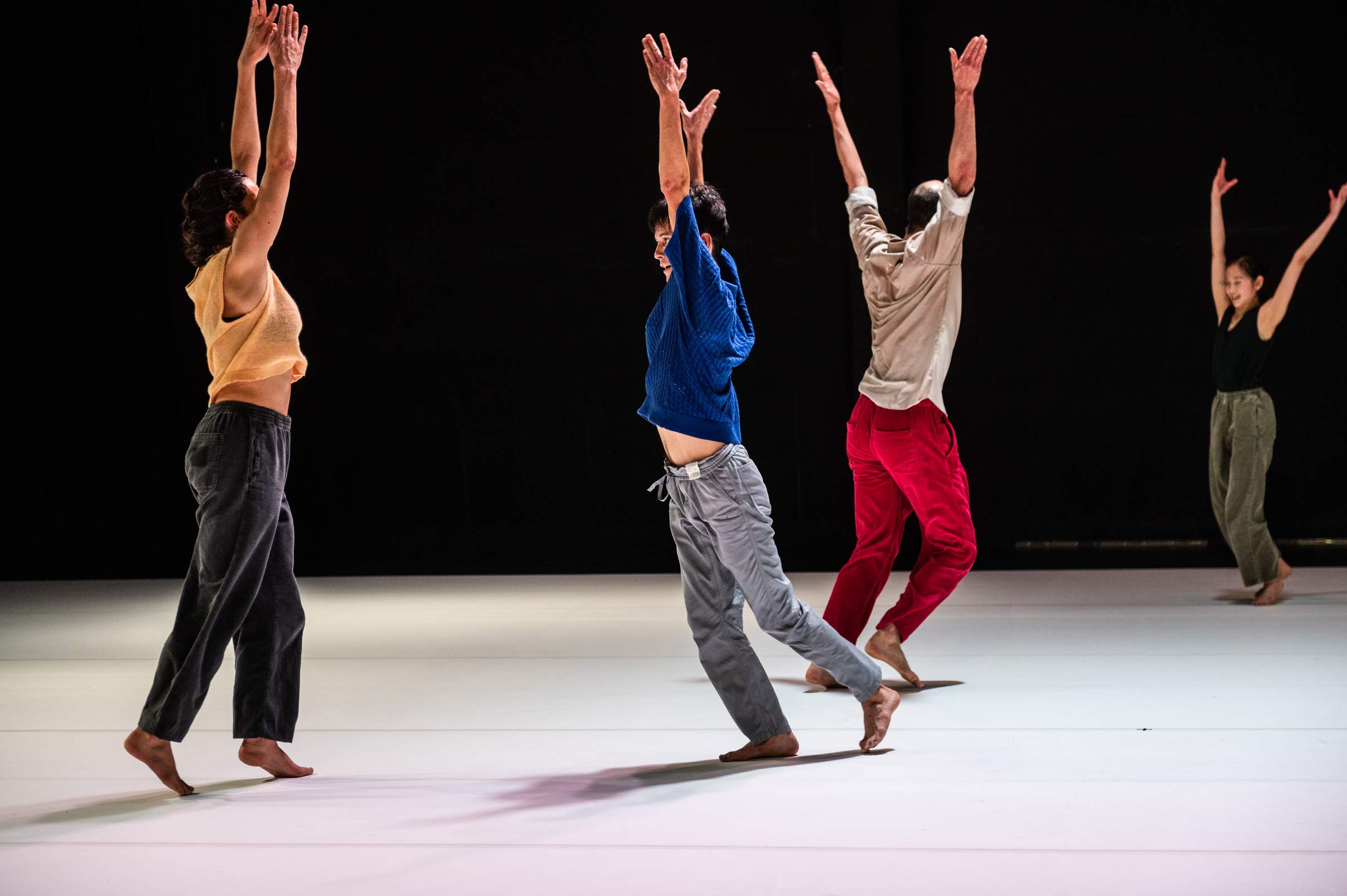 Four dancers raise their arms overhead in perfect unison during a joyful dance.