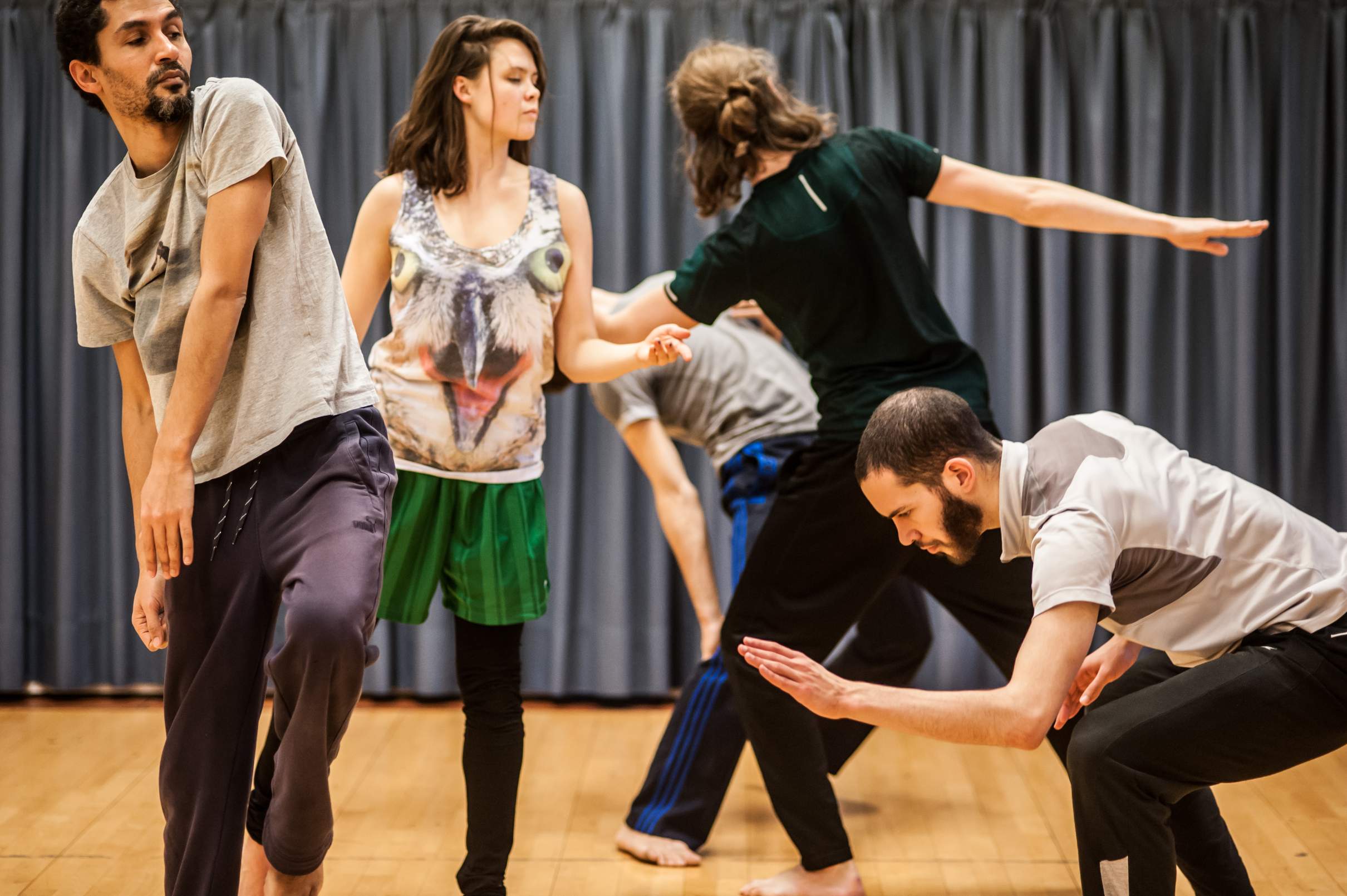Five dancers perform distinct movements and postures, closely intertwined in space.