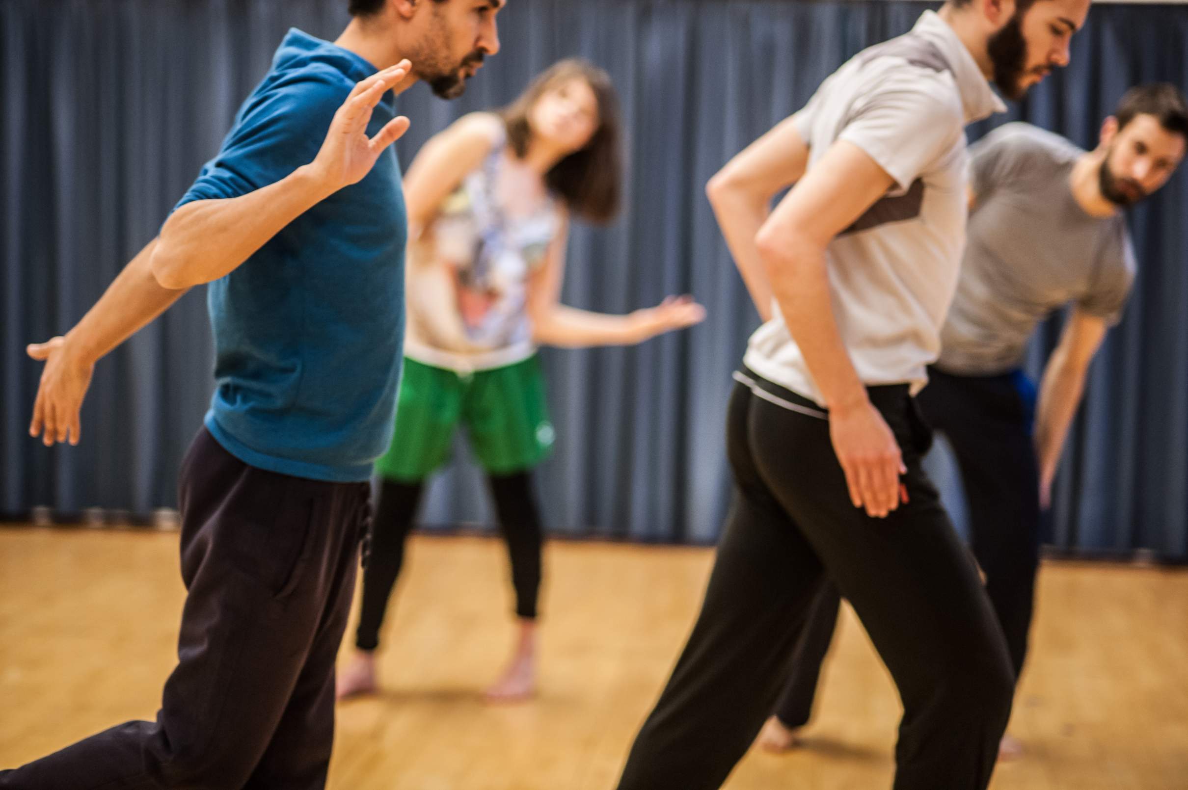 Four dancers lean to the right in synchronized tilt, their individual movements varying.