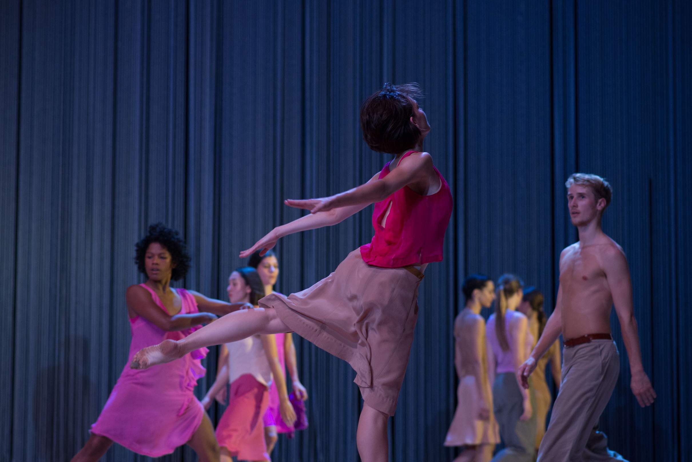 One dancer is caught mid-leap in the foreground, as others move in lines intersecting across the stage.