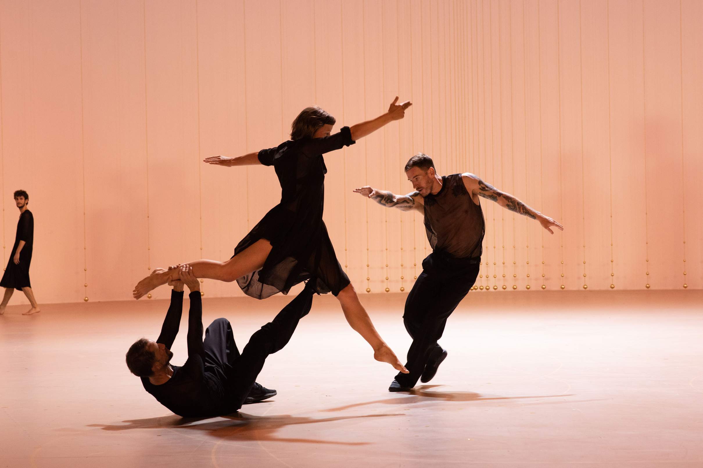 One dancer lies on the floor, supporting another dancer above him with arms and legs, as a third dancer moves alongside.