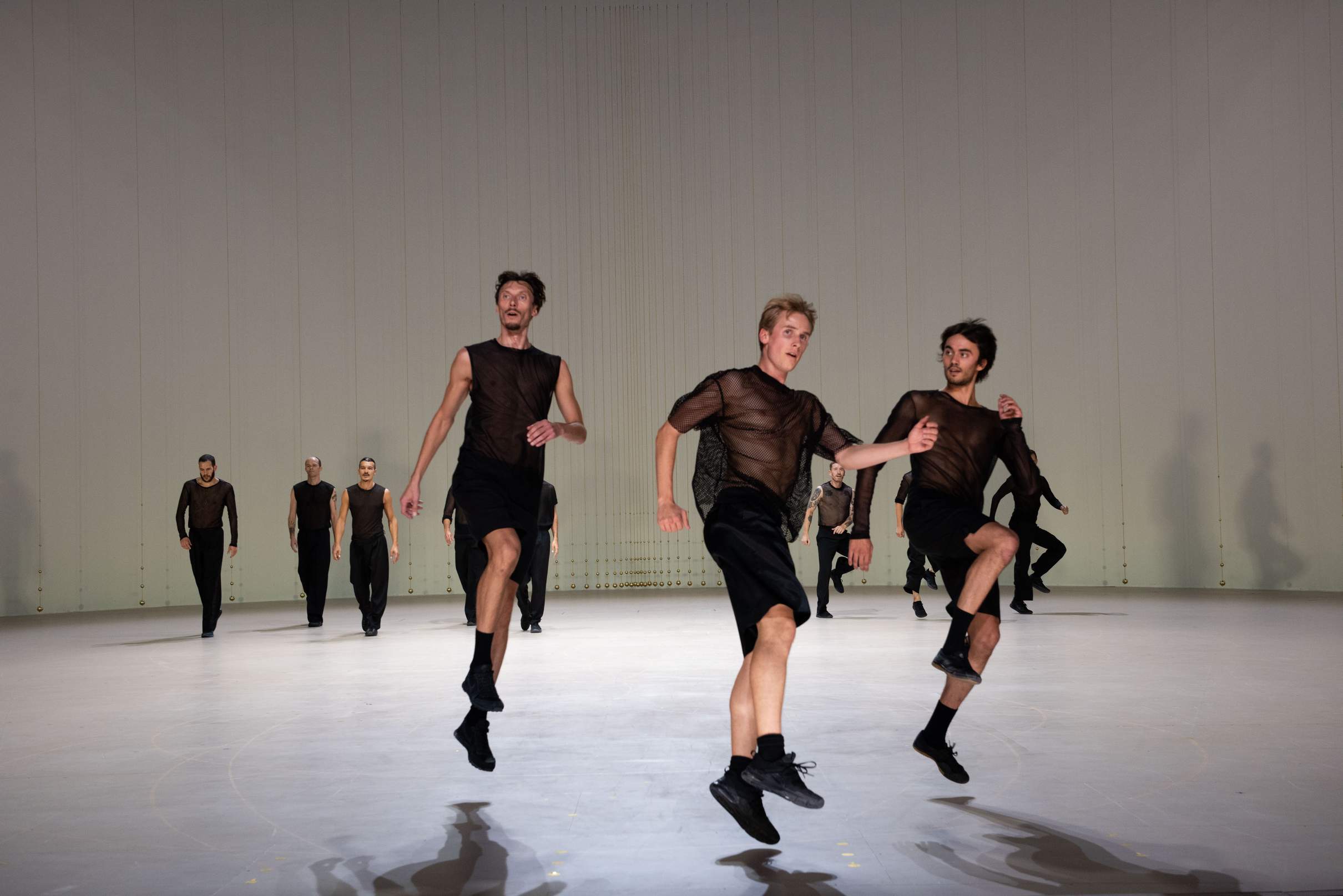 In the foreground, three dancers leap into the air, with two groups of dancers moving or skipping in the background.