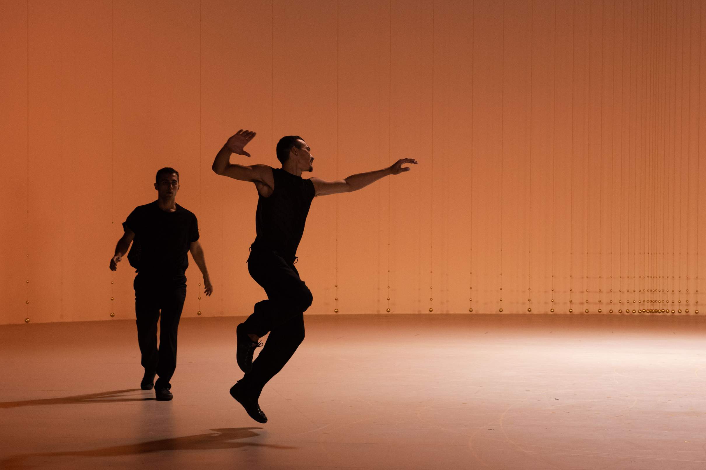 A dancer jumps across the stage, followed by another gathering momentum to jump.