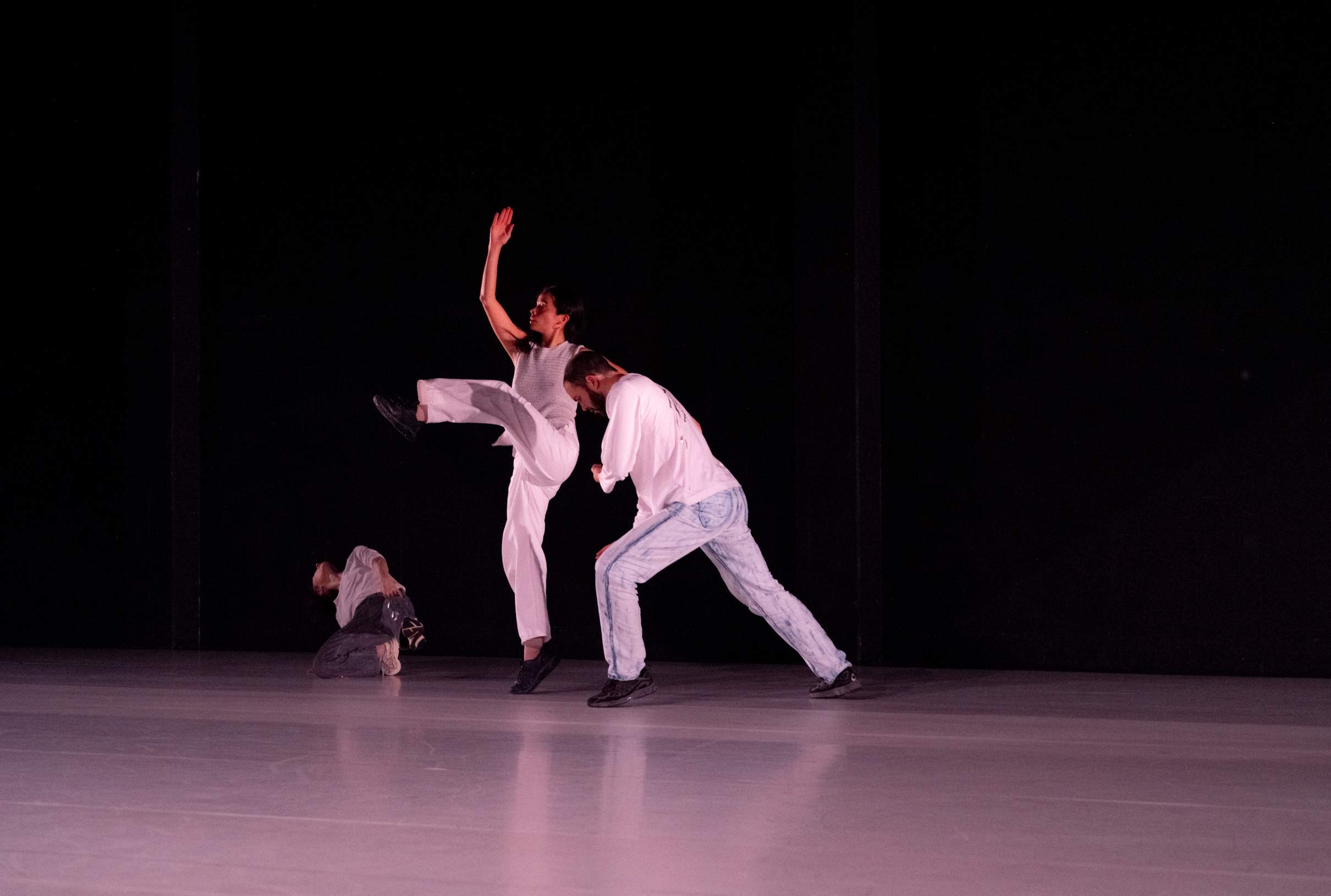 Three dancers reach outward into different parts of the space, their bodies stretching through broad, expansive motions.