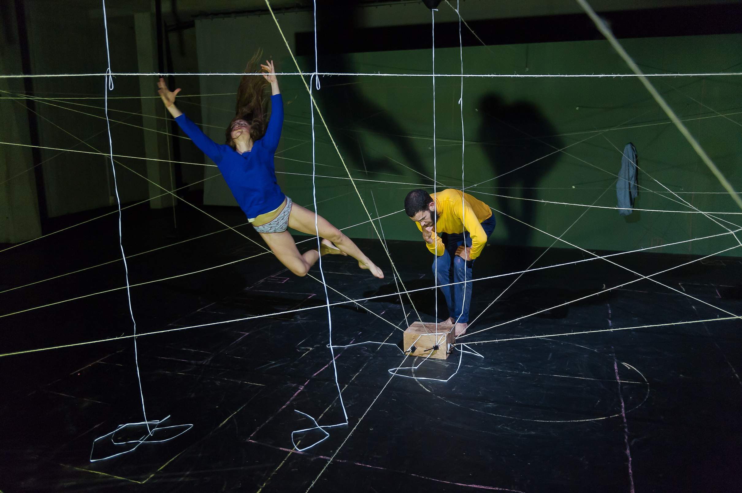 One actor flies through the air mimicking an explosion, while the other crouches in a thoughtful, awkward pose.